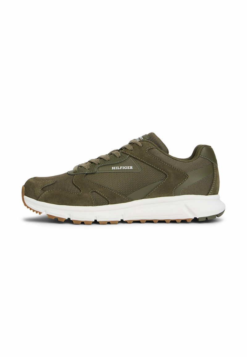 Zapatilla deportiva verde oliva con parte superior de malla, acentos de ante, suela blanca acolchada y suela de goma texturizada para mayor agarre. Logo de "Hilfiger" exhibido.