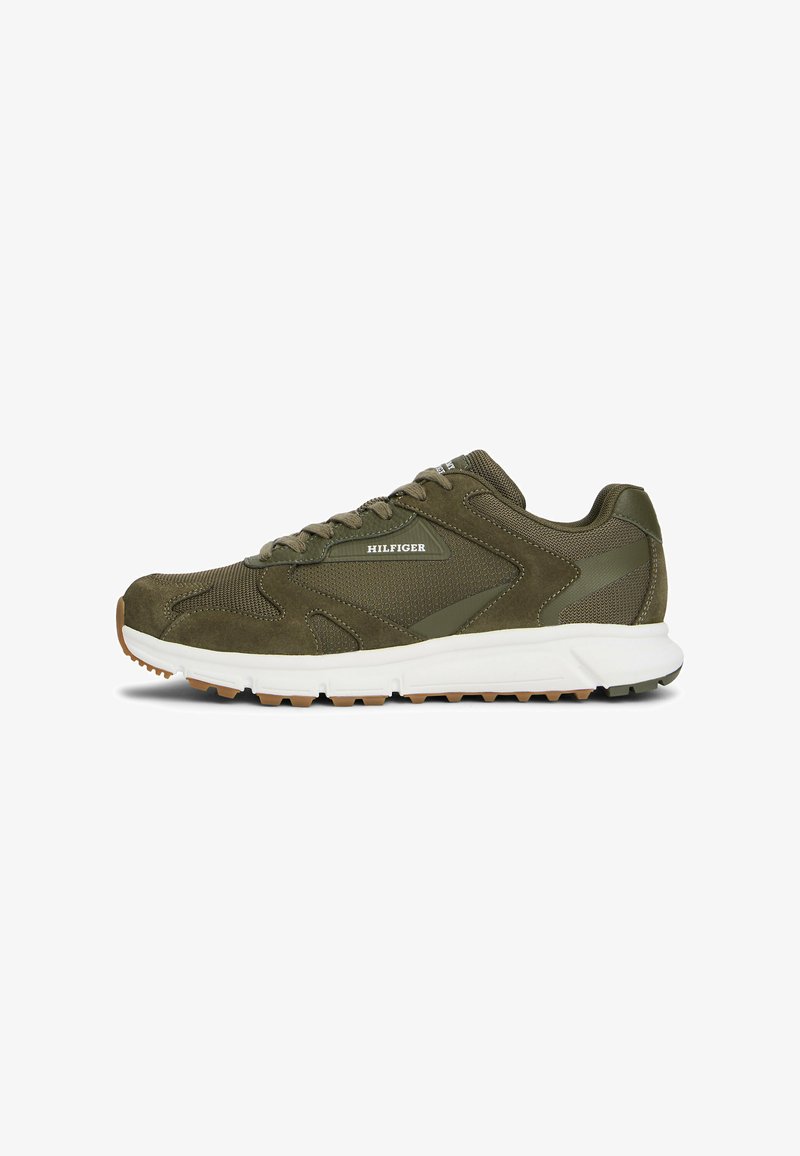 Zapatilla deportiva verde oliva con parte superior de malla, acentos de ante, suela blanca acolchada y suela de goma texturizada para mayor agarre. Logo de "Hilfiger" exhibido.