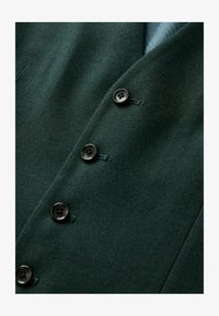 Blazer de lana verde oscuro que presenta cuatro botones negros, solapas ajustadas y una textura suave con detalles de costura sutiles.
