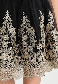 Svart kjol med intrikata gyllene broderier som visar blommor och vinrankor. Ett genomskinligt överdrag ger djup åt den texturerade tyget.