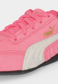 Baskets roses Puma avec lacets roses, bande latérale blanche, logo Puma doré et semelle noire sur fond blanc.
