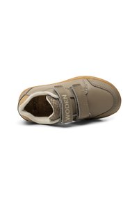 Beige lädersko med två kardborreband och en mjuk inre foder. Utrustad med en ljusbrun gummisula och "WODEN"-logotyp.