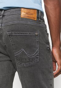 Šedé džínové kalhoty z denimu s koženou nášivkou značky, kontrastním bílým šitím a unikátním designem kapes s křivkovým detailem.