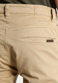 Khaki byxor med ett glatt bomullsmaterial, rak passform, bakficka med orange sömnad och en liten märkesflik.