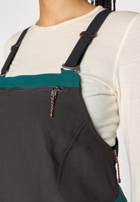 Μαύρες σαλοπέτες με τυρκουάζ λεπτομέρεια στην κορυφή, διαθέτοντας ρυθμιζόμενους μαύρους ιμάντες και μπροστινή τσέπη με φερμουάρ και πολύχρωμο λαβή.