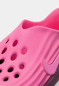 Jasnoružová nazúvacia topánka s viacerými ventilačnými otvormi a zvýšeným pätkovým uchom, s tonálnym logom Nike swoosh.