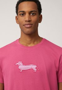 Camiseta de algodón rosa con un gráfico de un dachshund a rayas en blanco y rosa, con mangas cortas y cuello redondo.