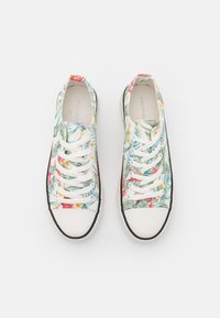 Canvas sneaker zijn versierd met een kleurrijk bloemenpatroon met groene bladeren en tropische bloemen, witte veters en een zwarte rubberen zool.