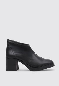 Bottine en cuir noir avec un talon bloc bas et un bout arrondi, présentée de profil sur un fond clair.
