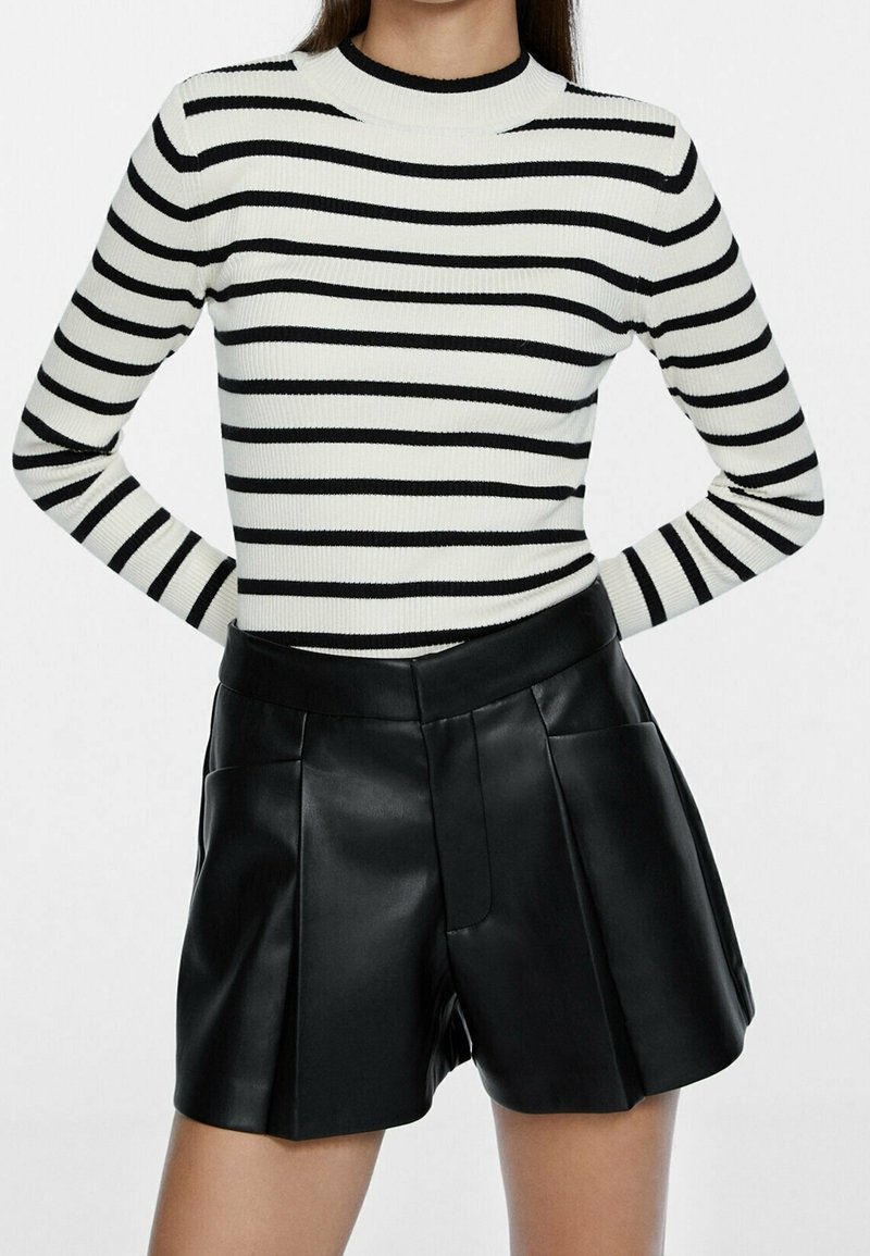 Femme portant un haut à manches longues rayé noir et blanc rentré dans un short en cuir noir plissé taille haute.