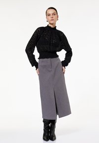 Sort blondedragt med rynket halsudskæring, parret med en tætsiddende grå nederdel med en frontslids, komplementeret af knæhøje sorte støvler.