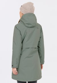 Grön vattentät jacka med huva och en skräddarsydd design. Har minimal hårdvara och en slät textur, tillsammans med en ljusbeige stickad mössa.