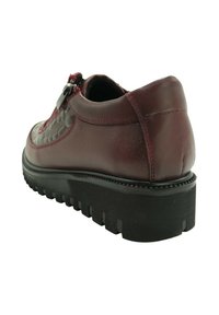 Zapato de cuero rojo oscuro con panel lateral texturizado, cremallera en el lado, suela gruesa negra estriada, visto desde un ángulo trasero izquierdo.