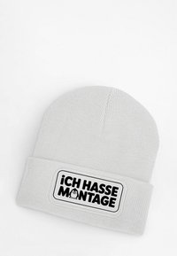 Light gray knit beanie with a folded cuff, featuring a black rectangular patch with the text "¡Ich hasse Montage!" and a cartoon penguin illustration.