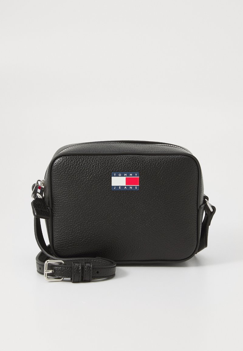 Zwarte leren schoudertas heeft een textuur oppervlak, een ritsluiting en een kleurlogo-patch met rode, witte en blauwe elementen.