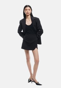 Blazer a righe nere sopra una canotta nera, abbinato a una gonna pantalone nera e scarpe con tacco nere. Tessuto liscio con linee eleganti.