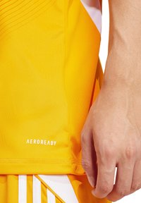 Gelbes sportliches Tanktop mit glatter Textur und runder Ausschnittform. Mit "AEROREADY"-Logo in Weiß und subtilen Linienmustern auf dem Stoff.