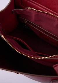 Interno di una borsa a mano in pelle rosso scuro con diversi scomparti, inclusa una tasca con zip e denti della zip in tonalità oro.