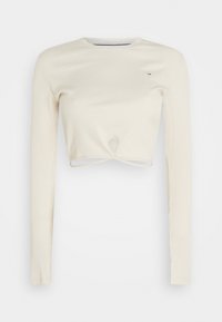 Beige ribbat långärmad crop top med rund hals och liten nyckelhålsöppning framtill, med en liten logotyp på bröstet.