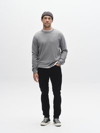 Siva majica dugih rukava s okruglim izrezom na vratu, u kombinaciji s crnim hlačama i crno-bijelim tenisicama. Bijela potkošulja i siva pletena kapa.