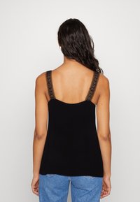 Top nero senza maniche con delicati dettagli in pizzo sulle spalle, caratterizzato da una vestibilità rilassata e una texture morbida, che si abbina a jeans blu.