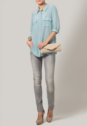 Woman wearing light blue blouse, gray skinny jeans, beige high heels, and holding a beige clutch bag with a chain strap.