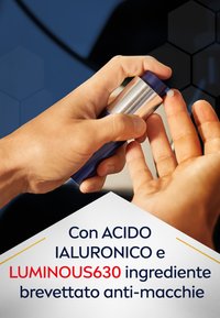 Bottiglia spray blu e argento tenuta sopra una mano con una piccola goccia di crema bianca su un dito. Il testo promuove l'acido ialuronico e LUMINOUS630.
