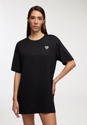 T-shirt nera oversize realizzata in tessuto morbido. Presenta una piccola grafica a forma di cuore argentato sulla parte sinistra del petto. Maniche corte e scollo rotondo.