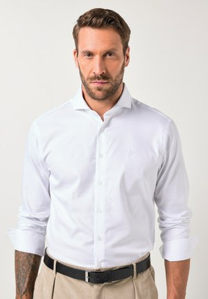 Camisa blanca de botones de tela suave, con un cuello clásico, mangas largas y un sutil bordado de "JP" en el pecho.