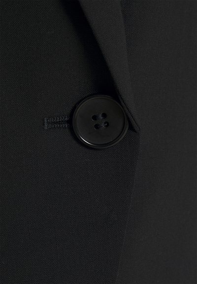 Blazer de tecido negro com um botão preto brilhante de quatro buracos. A textura é suave com um design estruturado.