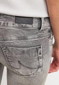 Jean en denim gris avec une finition texturée, patch logo LTB et une poche arrière ornée de deux clous métalliques noirs.
