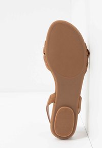 Sandale marron avec une semelle en caoutchouc flexible, un pied moulé, et des sangles ajustables élégantes. Surface texturée avec un design minimaliste.