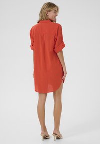 Robe chemise en lin rouge avec des manches courtes retroussées, détails de pli au dos, ourlet incurvé et coupe décontractée.