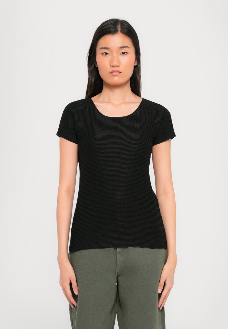 Black, short-sleeved top with a textured knit design and a round neckline, paired with olive green pants.