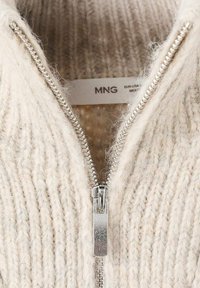 Maglione lavorato a maglia color beige chiaro con chiusura a zip argentata, modelli testurizzati e un'etichetta con il nome del marchio "MNG."