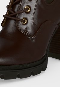 Gros plan d'une chaussure en cuir poli marron foncé avec des œillets dorés, des lacets marron et une semelle épaisse noire à crampons.