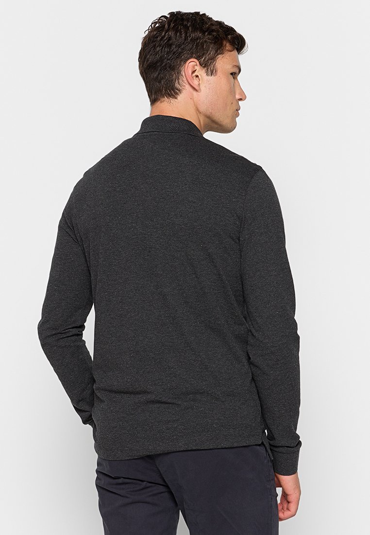 Polo à manches longues de couleur gris foncé fabriqué en tissu doux. Il possède un col et une texture subtile. La vue de dos montre un design ajusté avec des fentes sur les côtés.