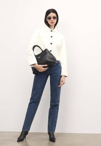 Chaqueta blanca corta con botones negros, jeans de mezclilla azules y botines negros de tacón. Bolso negro sujetado con la mano derecha.