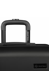 Asa retráctil extendida en maleta rígida negra con superficie texturizada y marca SMARTBOX en el asa y en la parte frontal de la maleta.