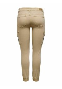 Beige cargobyxor med en figurnära design, elastiska ärmslut, bakfickor och sidofickor med svarta accenter. De är tillverkade i ett elastiskt bomullsblandat material.