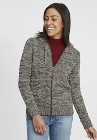 Grå stickad zip-up tröja med huva, med ribbade detaljer och träknappar, i kombination med en vinröd topp och jeans.