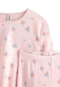 Completo pigiama con tessuto rosa tenue, motivo floreale in rosso, blu e verde, con scollo rotondo e pantaloni a vita elasticizzata.