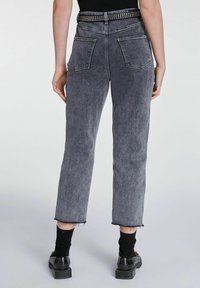 Jeans in denim grigi con vita alta, dal look sbiadito, con tasche posteriori e orlo sfilacciato, abbinati a una cintura nera con borchie.