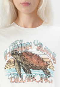 Hvit bomulls t-skjorte med et fargerikt grafisk motiv av en skilpadde, tekst som sier "Besøk de hawaiianske øyene," og "Billabong"-logoen nederst.