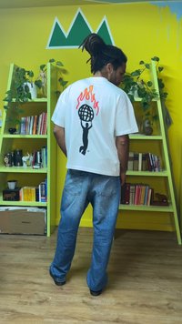 White short-sleeve t-shirt with a black flame design and a globe graphic on the back. Worn with blue denim jeans in a colorful interior.