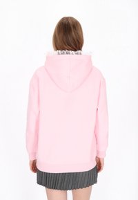 Sudadera con capucha rosa con un ribete texturizado de volantes en el cuello, mangas largas y un ajuste regular, combinada con una falda gris plisada.