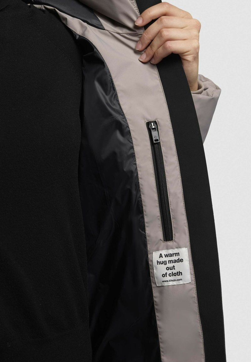 Tissu extérieur noir avec une doublure intérieure gris clair ; doté d'une fermeture éclair et d'une étiquette en tissu indiquant : "Une étreinte chaleureuse faite de tissu."