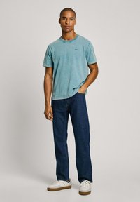 Světle modré bavlněné tričko s kulatým výstřihem a krátkými rukávy v kombinaci s tmavě modrými džíny. Tenisky s bílými a hnědými akcenty.