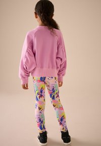 Rózsaszín, oversized pulcsi puffos ujjakkal, színes, virágmintás leggingsekkel párosítva. Fekete, magas szárú tornacipővel egészítve ki a megjelenést.