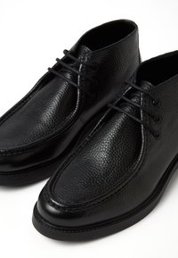 Scarpe in pelle nera con finitura testurizzata, punta arrotondata e lacci sicuri. La suola è piatta, contribuendo a un design classico.